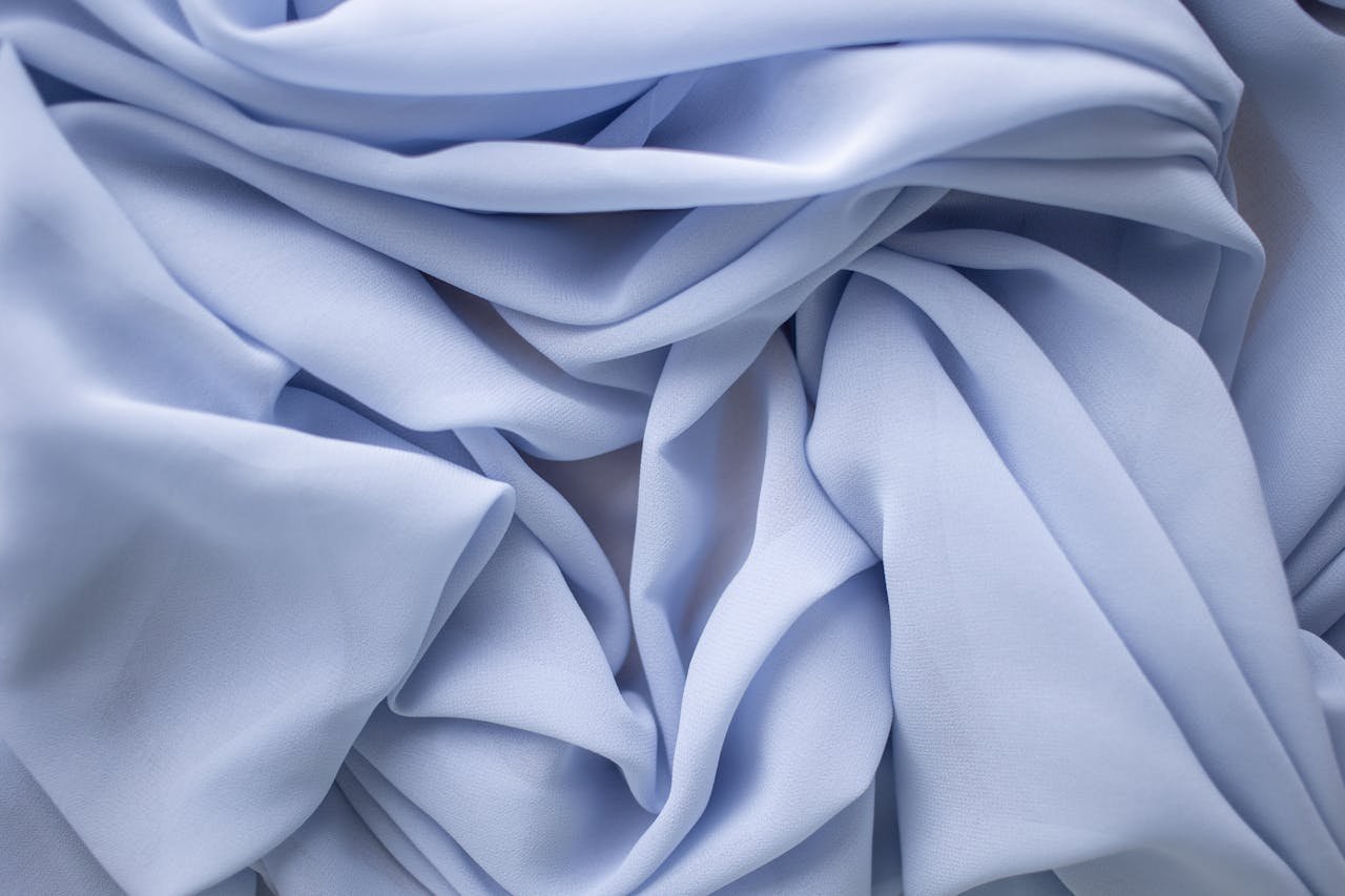 Close-up of light blue fabric with elegant folds and delicate texture, perfect for backgrounds.